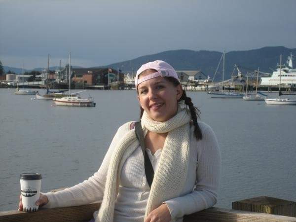 Girl in braids, wearing a pink baseball hat, white scars, and white sweater, with Bellingham, Wa and water in the background. I wasn't as scared to travel when I had a friend along.