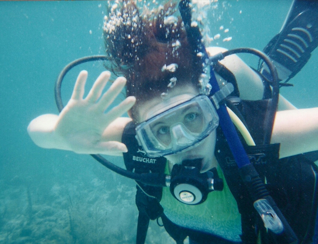 Dark haired woman, underwater and waving while wearing scuba gear. No scuba diving accidents on this day!