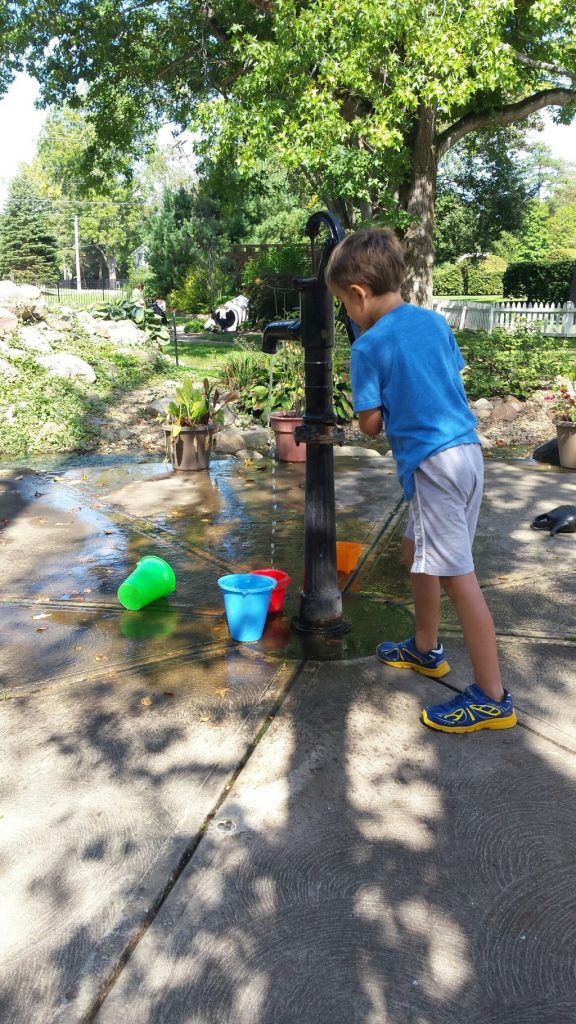 A child pumping water into a colorful bucket