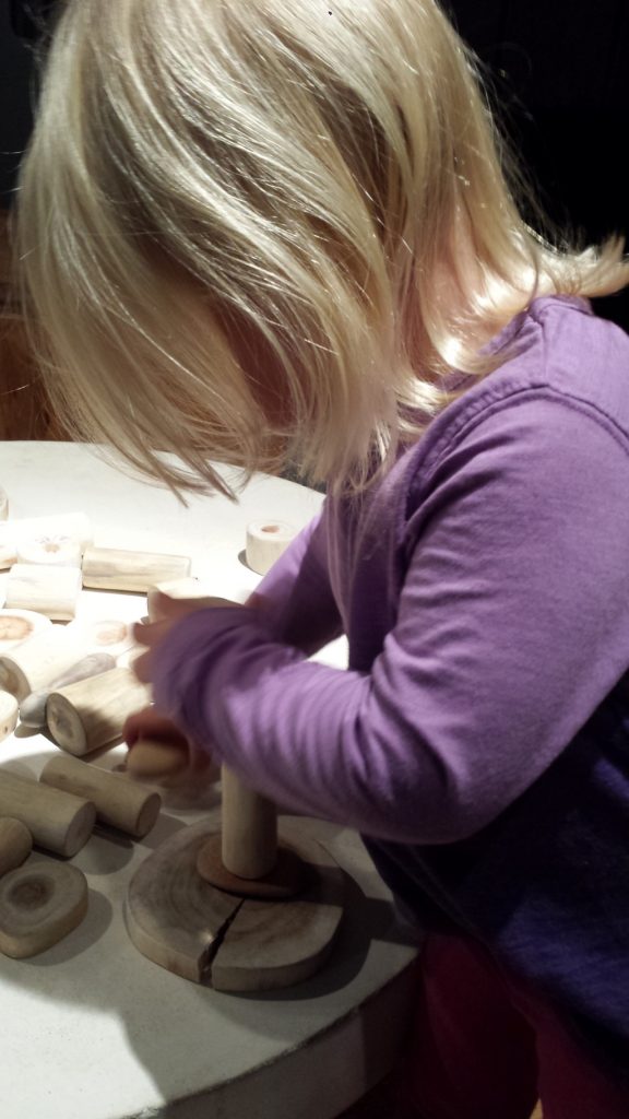 Child playing with wooden pieces to make a sculpture of sorts.