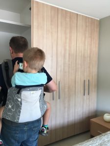 A picture of a man wearing an older child on his back in a carrier while house hunting. 