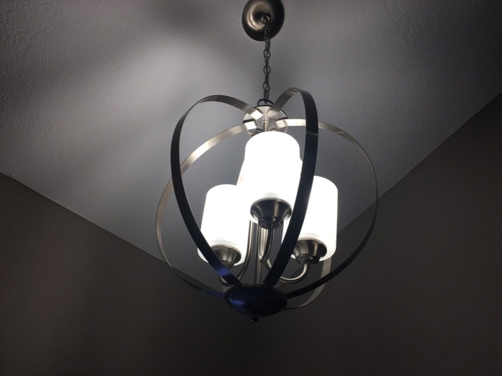 A picture of a silver hanging light fixture with the lights on in the post the storm before the calm. 