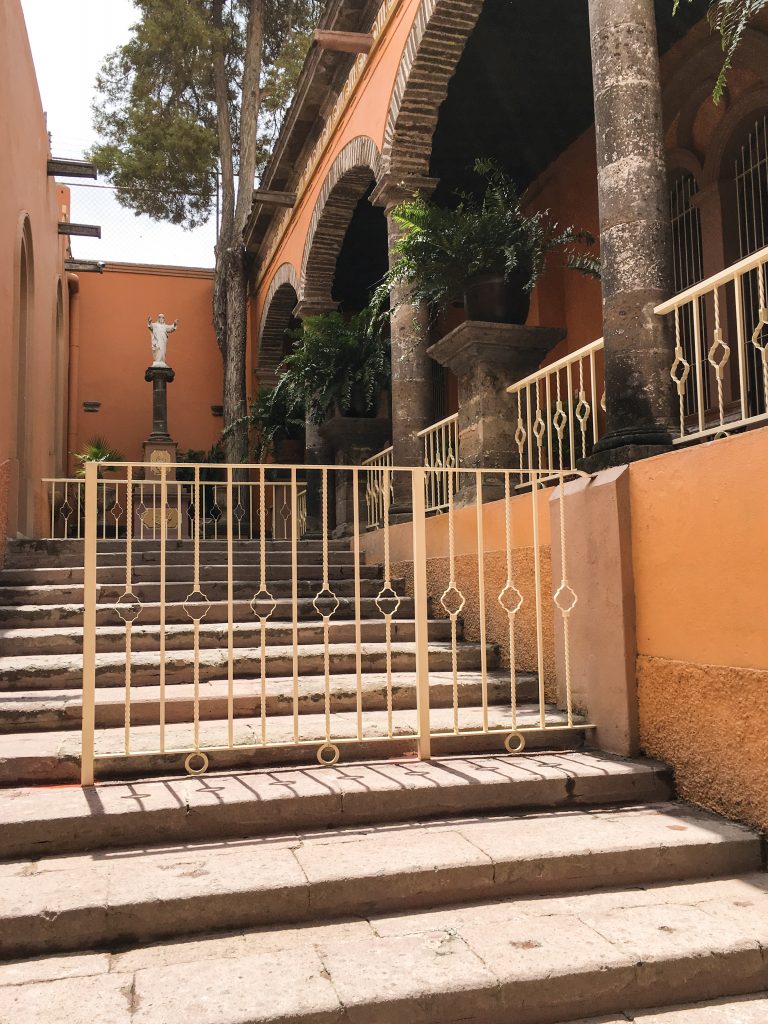 A private area outside of a huge, beautiful church. It has arched columns, stairs and the color is a vibrant orange