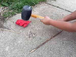 A child's arm is shown, holding a rubber mallet. There is a flattened red mega block about to be hit again with said mallet.