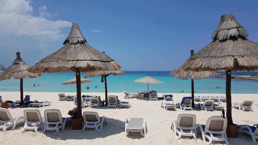 Pictured: a beach with lounge chairs, permanent thatched umbrellas, leading to the turquoise ocean water.