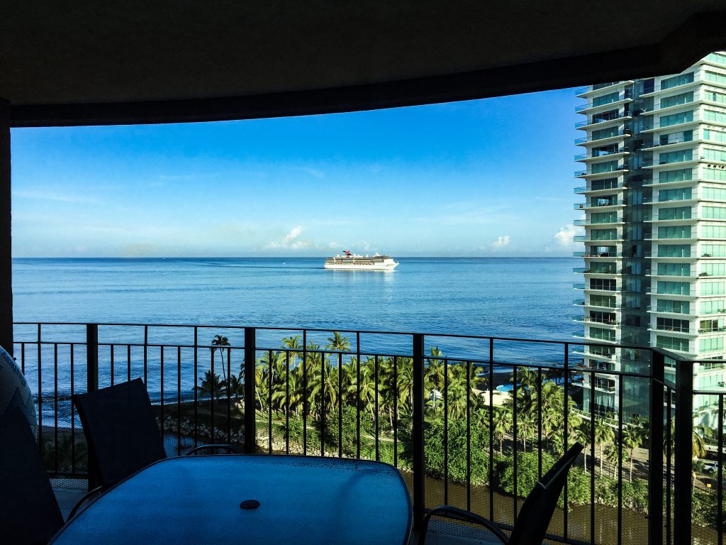 A balcony with a view of the ocean and a ship on the horizon, during the day