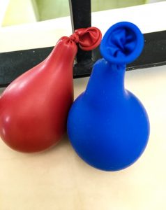 a red balloon and a blue balloon, filled with cornstarch, with wrought iron behind them.