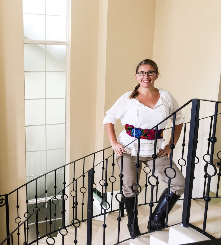 A woman stands on a staircase in a homemade pirate costume, including brown knee high boots, and a Mexican belt that's flowery.