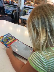 a little girl in a green and white striped shirt draws on a reusable, magnetic pad.