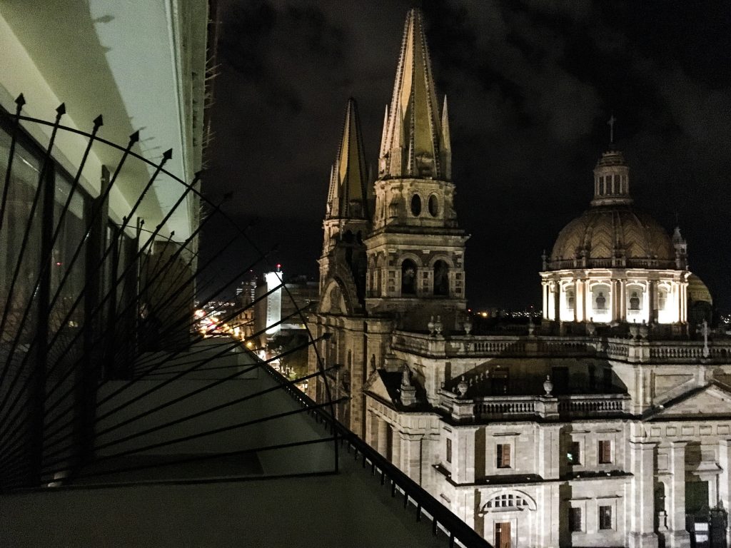 from a balcony, with ironwork at eye level on the left, and a beautiful church lit up on the left.