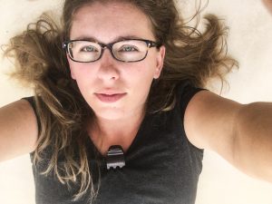 a picture of the author, wearing glasses and laying down on white tile. Her hair is light brown and a mess around her.