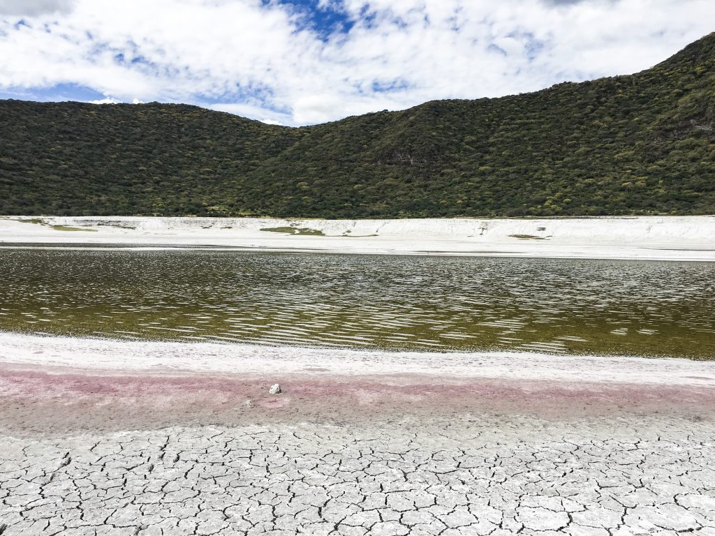 small lake with greenish, bronwish water that is red around the edges from inside the crater