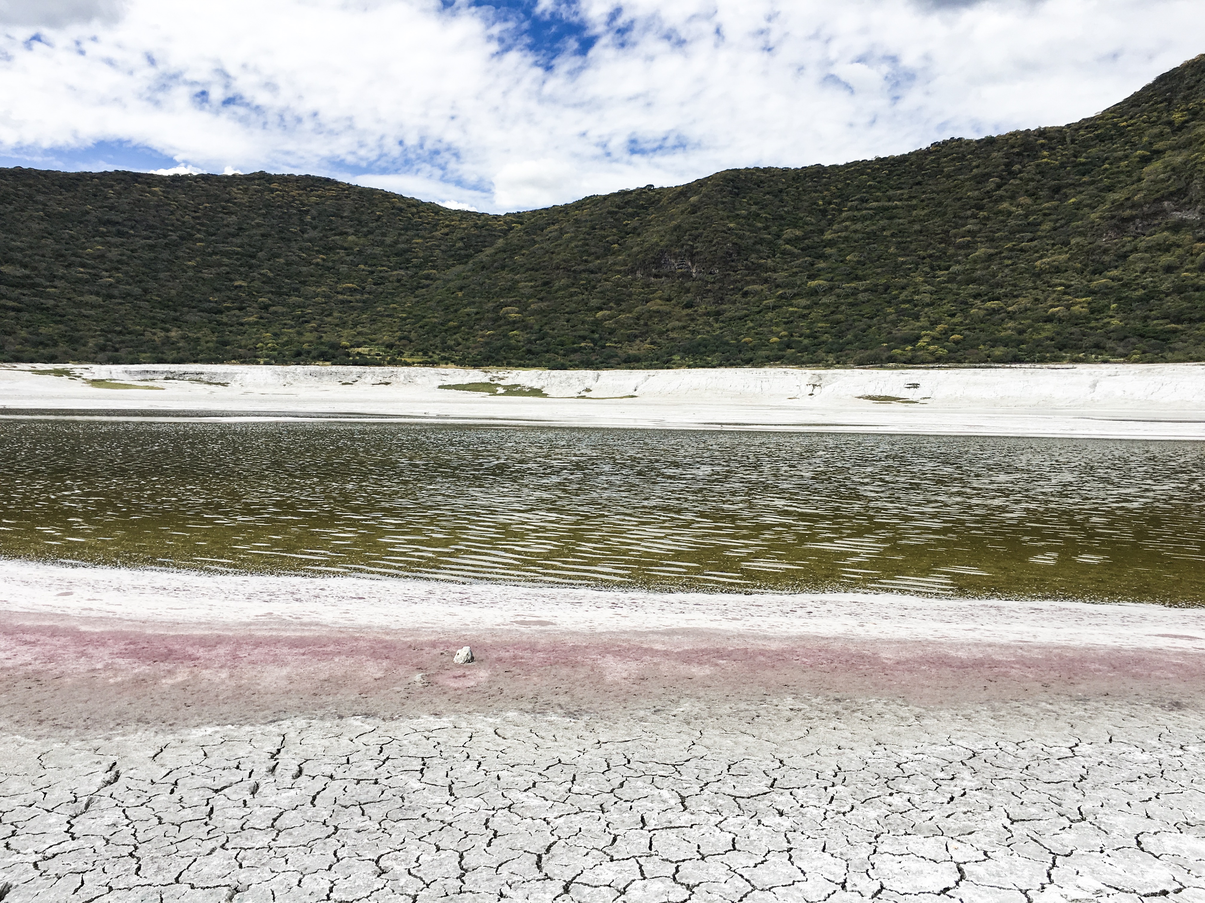 small lake with greenish, bronwish water that is red around the edges from inside the crater