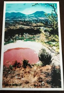 a picture of a postcard and on it is an old picture of when the crater was filled with water. In this picture, the water is a reddish pink color (likely caused by algae)