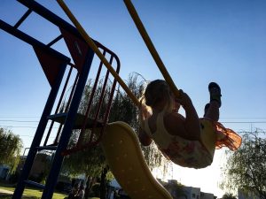 the silhouette of a girl swinging high on her swing.