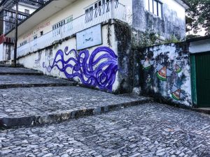 Wide stone "stairs", with artwork on the wall in the background. It is a large, purple octopus.