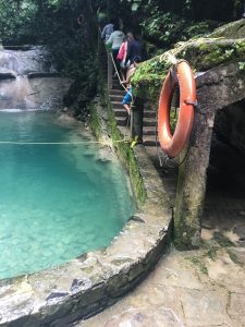 a blue, natural pool on the left and steps on the right. An orange life preserver hangs on a wall in the foreground (there is a tunnel to get to the stairs, on the far right)