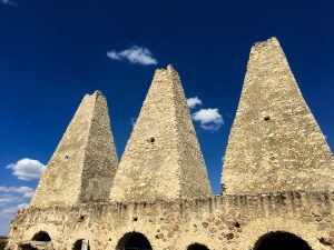 a graying trio of off-white stone towers made of stone, against a deep blue sky with few clouds at the Santa Brigida Mine