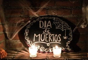 a spooky sign covered with cobwebs that says "Dia de Muertos." In front sit two white, lit candles. This from our first Day of the Dead party.