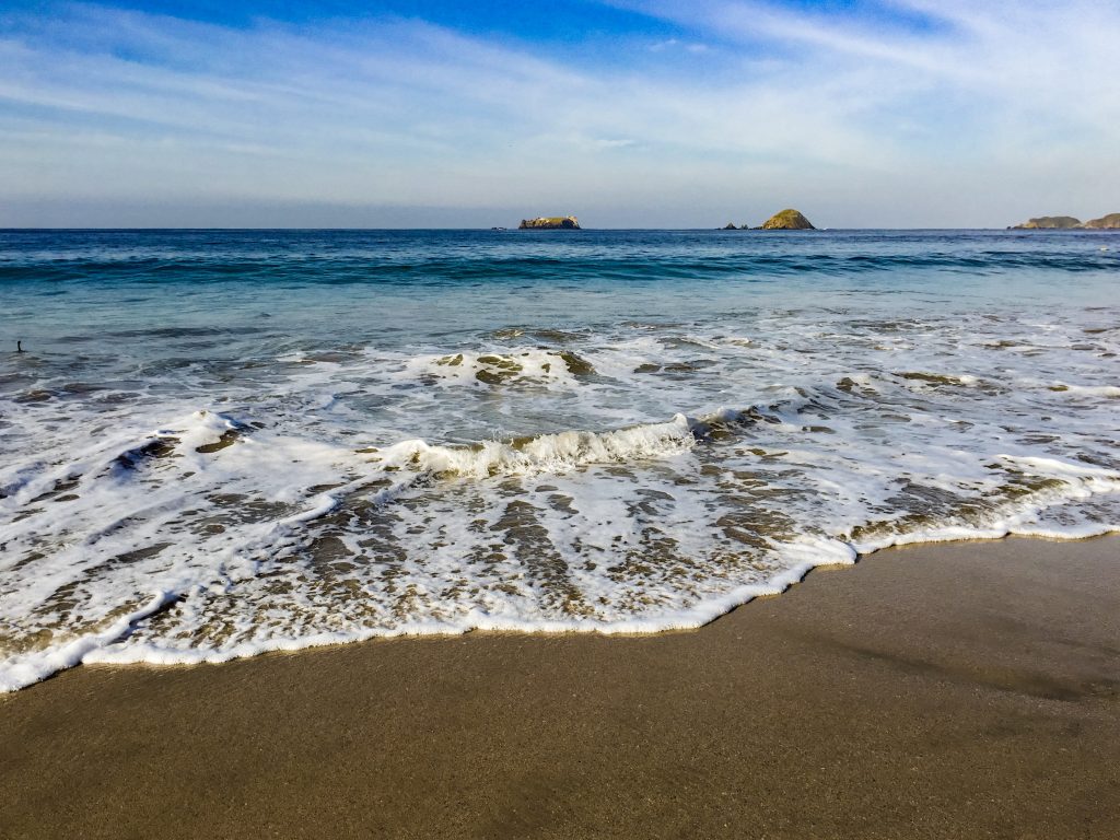 A wave coming up the sand, with the ocean in a deep blue in the background