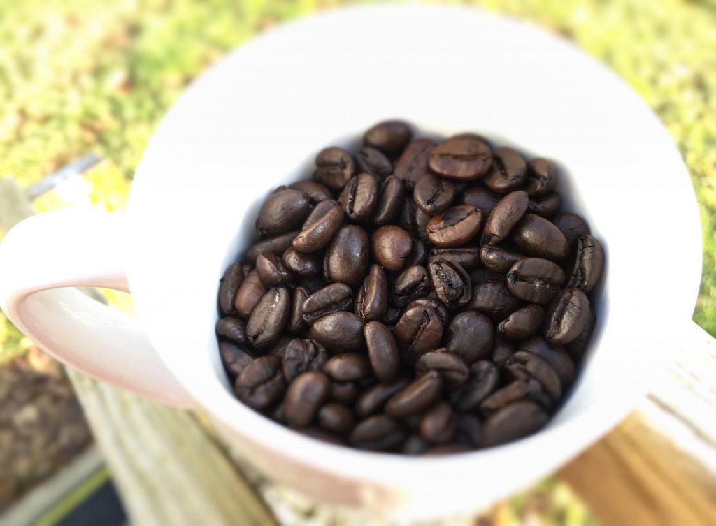 a brilliant white cup filled with coffee beans, sits on a wooden post (barely visible) and there is a bit of greenish grass in the background. I'm trying to make small changes and travel more.