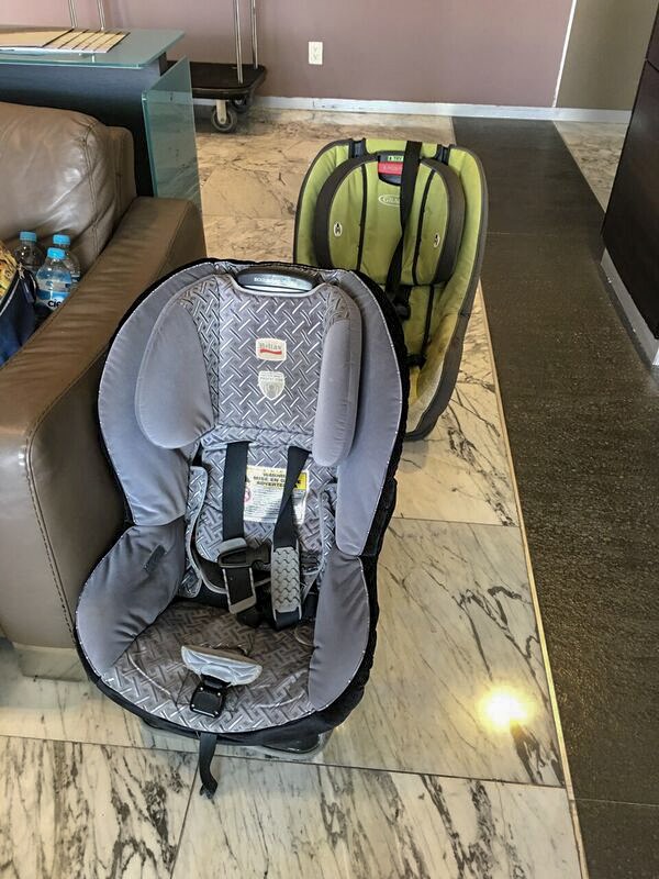 Two car seats sit on the ground in a hotel room. Yes, we were always flying with car seat in airplane (times 2)! Are these the best travel car seats? Read on!