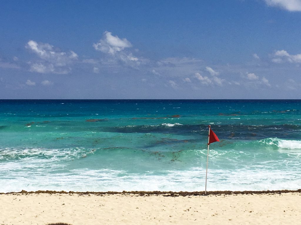 A beach with turquoise waters in the background. The right third contains a red flag. It was the end of our road trip Yucatan.