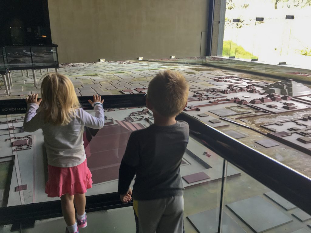 two children are on a bridge, looking over a model of the Teotihuacan site. In front of them is the Temple of the Sun and off to the far right is the Temple of the Moon.