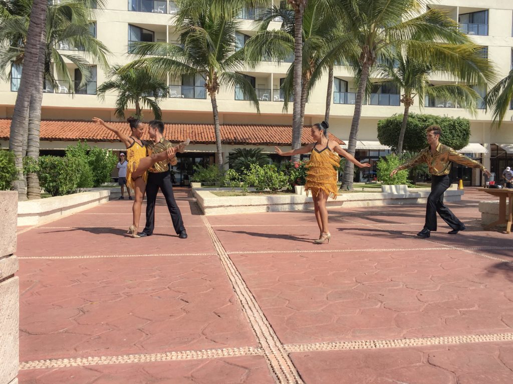 Four dancers, two male and two females wearing yellow and black, dance on the red bricks in front of palm trees at the Barcelo Ixtapa. A great mexico all inclusive with kids!