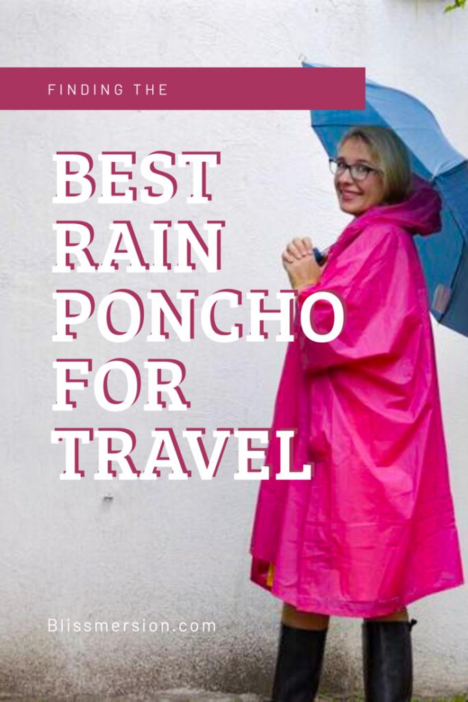 Finding the best rain poncho for travel - a woman wearing a pink pocho, black rubber boots, and holding a blue umbrella is featured against a white wall.