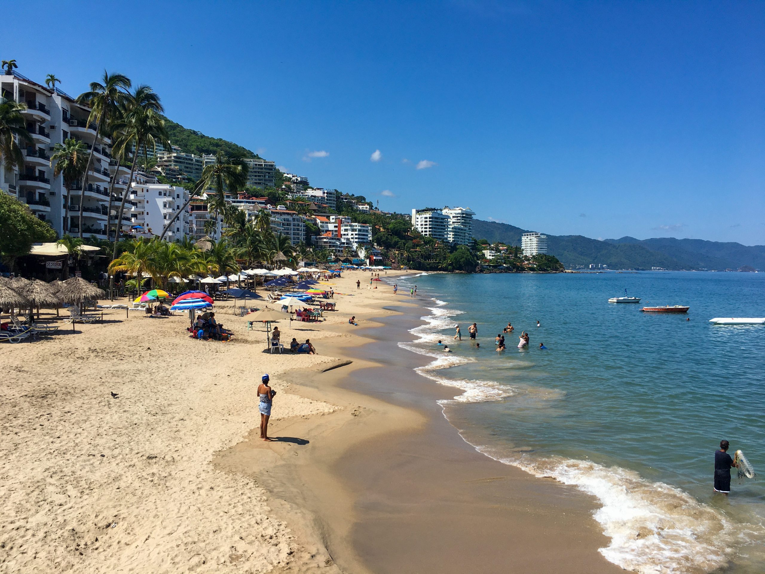 a tan sand beach, with the ocean on the right and the buildings of Puerto Vallarta on the left.