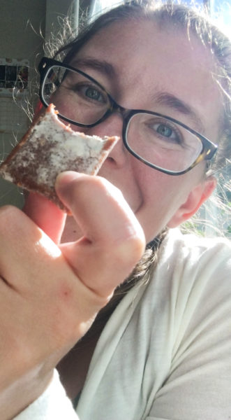 A woman wearing glasses, holds a piece of brown soft candy dusted with white powder. It's pulparindo and it's one of the best Mexican candy options!