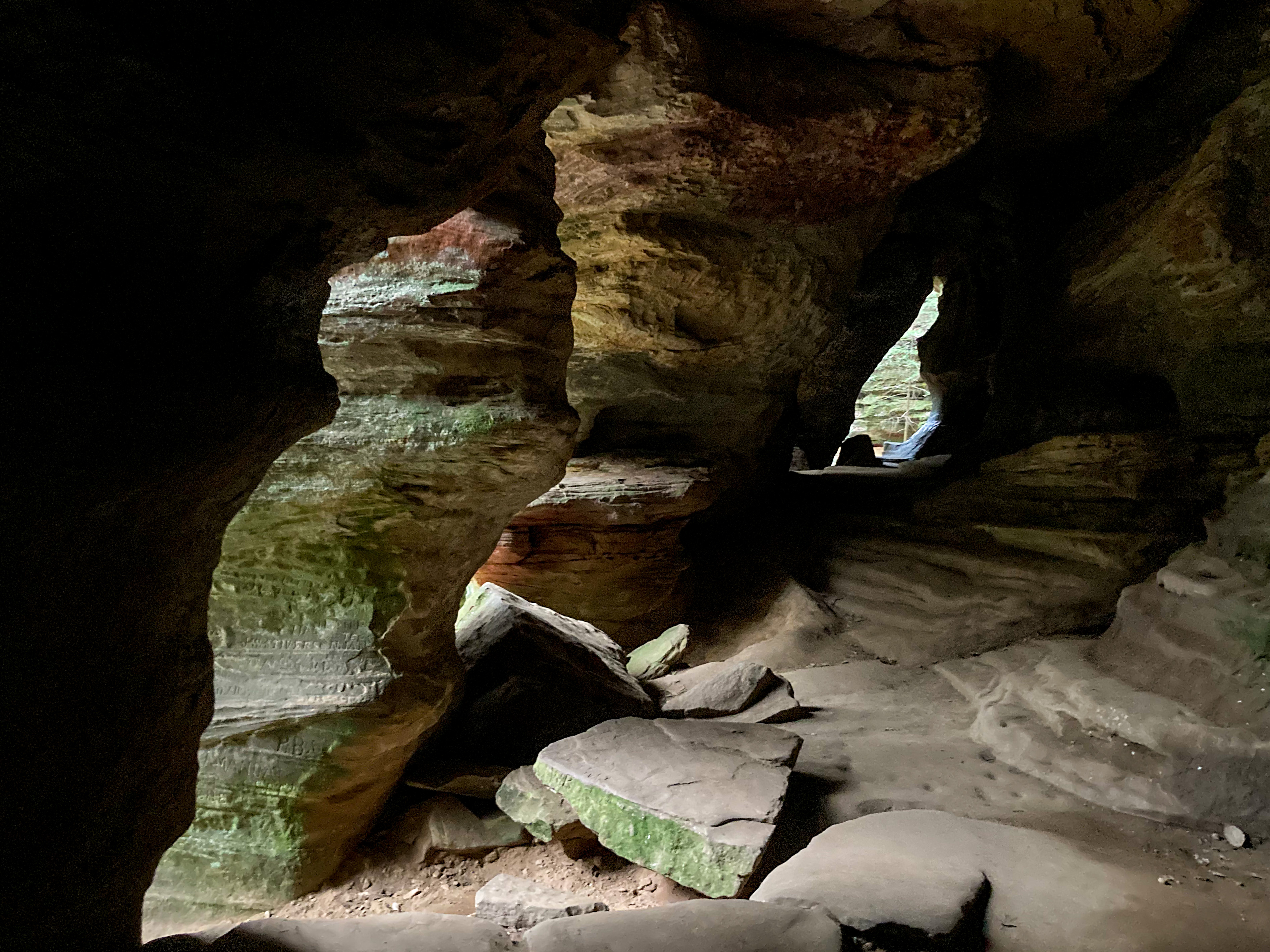 The inside of the Rock House cave. There is an odd shaped opening at the far end and two openings along the side to provide light inside. The left side of the photo is so dark, that you cannot see the texture of the rock, only the outline.