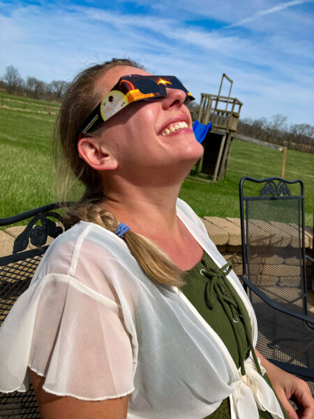 a woman peers up to the sky wearing solar eclipse glasses.